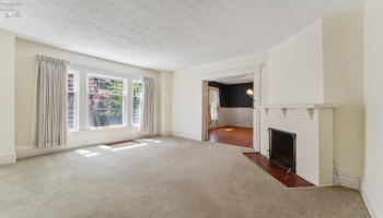 Central living room with expansive south-facing windows and fireplace. Hardwood floors underneath in good shape per owner.