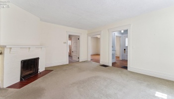 Central living room with expansive south-facing windows and fireplace. View looking into formal dining room. Hardwood floors underneath in good shape per owner.